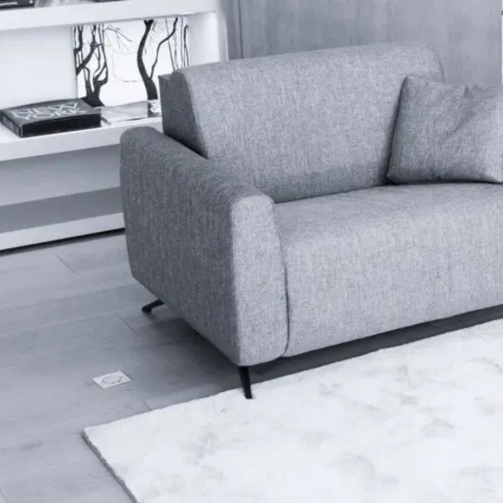 A modern two-seater sofa in textured light gray fabric, shown in a minimalist living room setting with a white rug, gray floor, and a white shelf in the background.