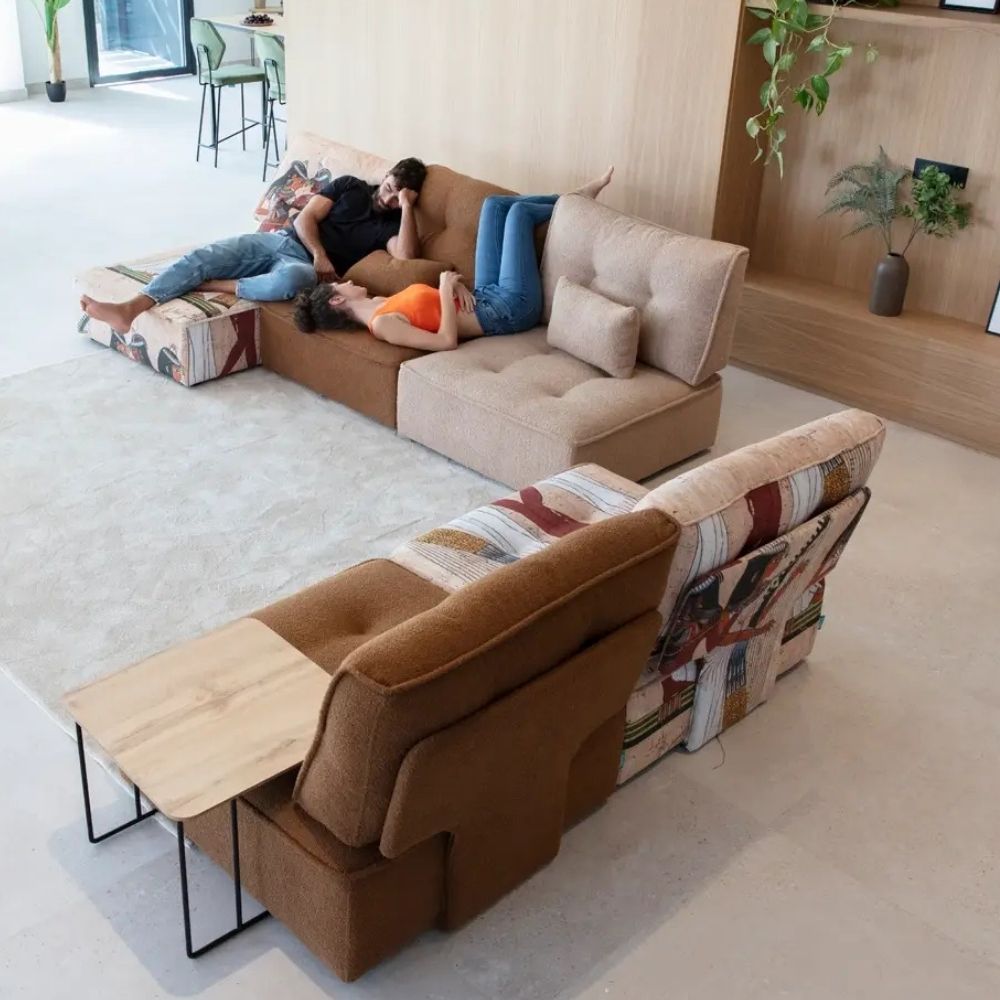 A modern sectional sofa set in a bright, minimalist living room. One section is upholstered in a warm brown fabric with a striped and floral patchwork pattern on the outer armrests, while the other section is a light beige tufted fabric.