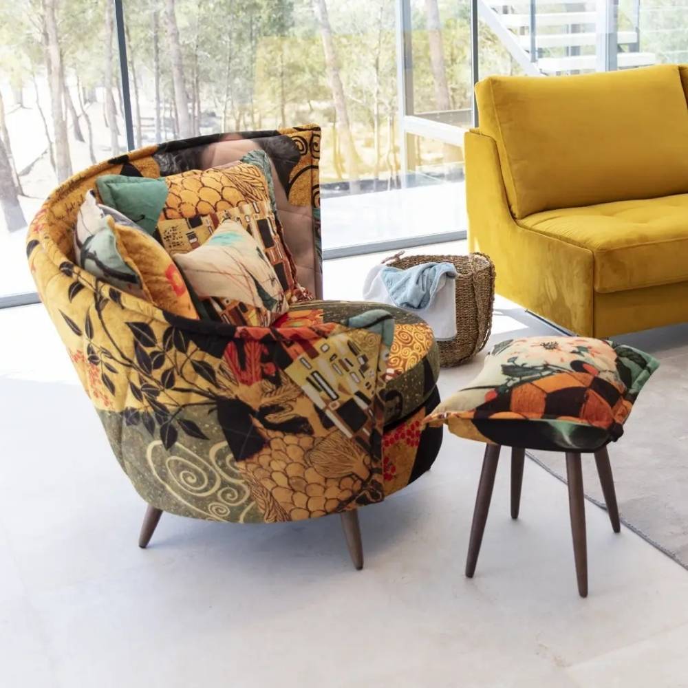 A mid-century modern accent chair and matching footstool with a complex multicolor patchwork floral and geometric pattern, styled in a bright living room next to a yellow sofa.