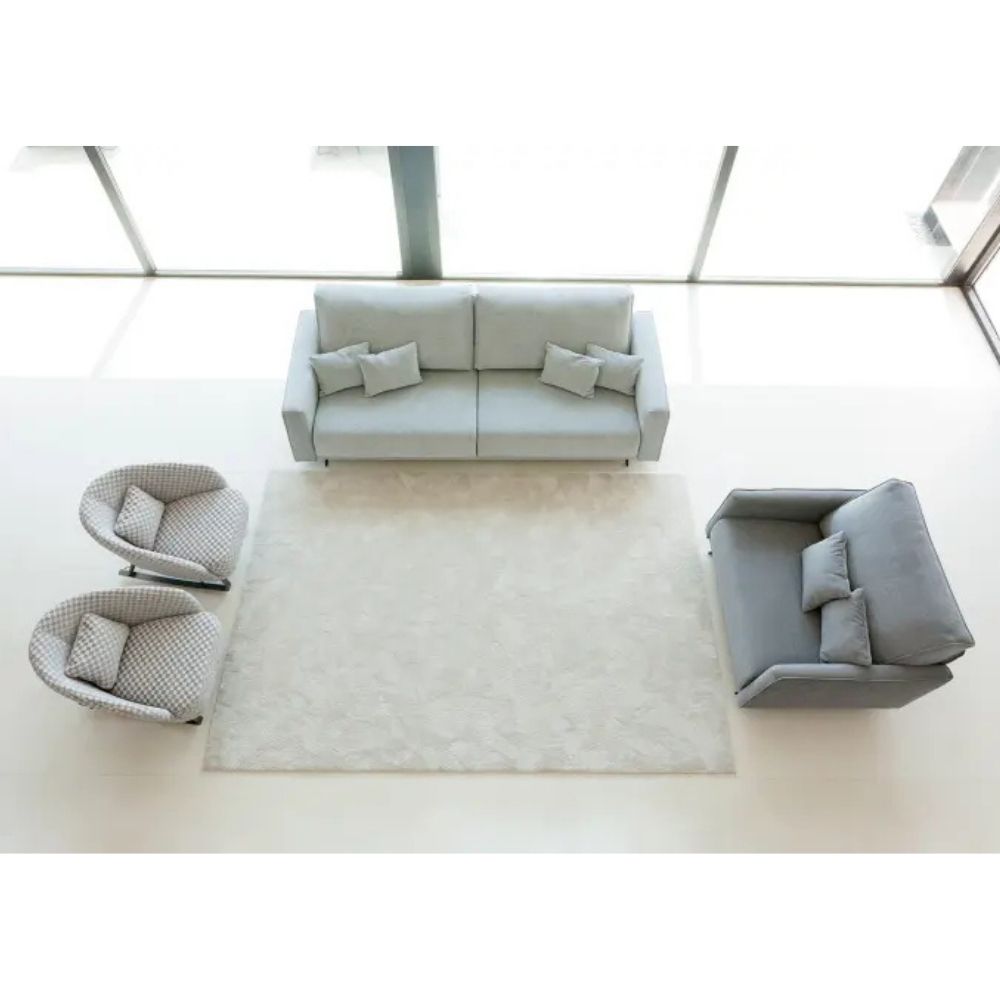 A modern living room setup featuring a light gray three-seater sofa, a matching two-seater loveseat, two round armchairs with patterned upholstery, and a large rectangular shag rug on a light floor.