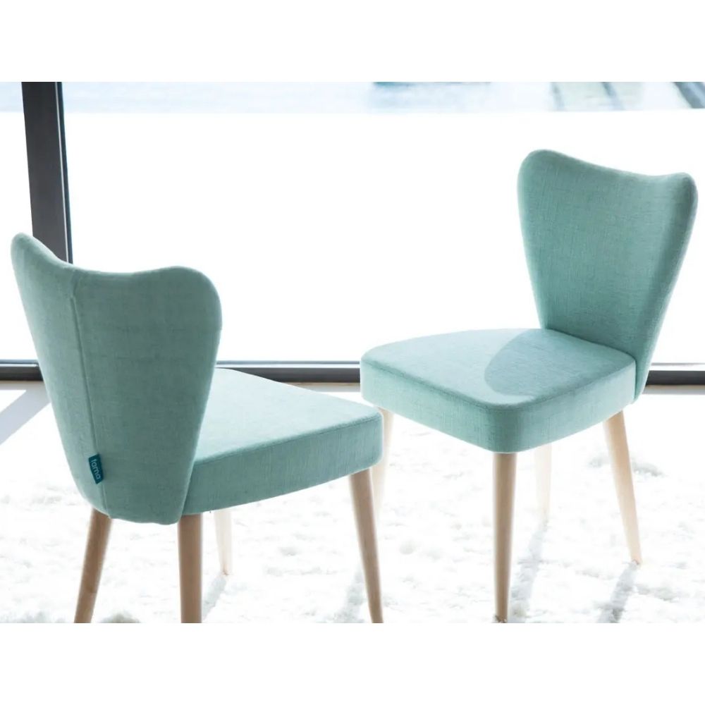 Two upholstered dining chairs in a light mint green fabric with light wood legs, shown in front of a bright window.