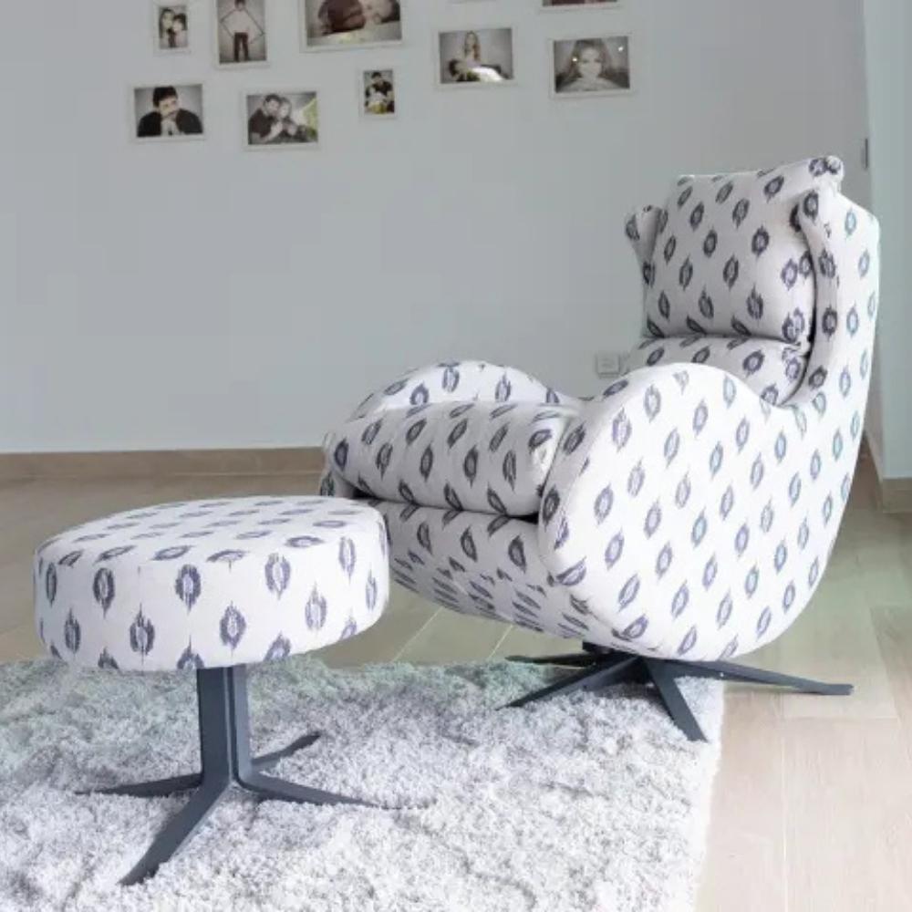 A white upholstered lounge chair with a matching footstool, both featuring a gray geometric ikat pattern, set in a modern living room with a white shag rug and light wood flooring.