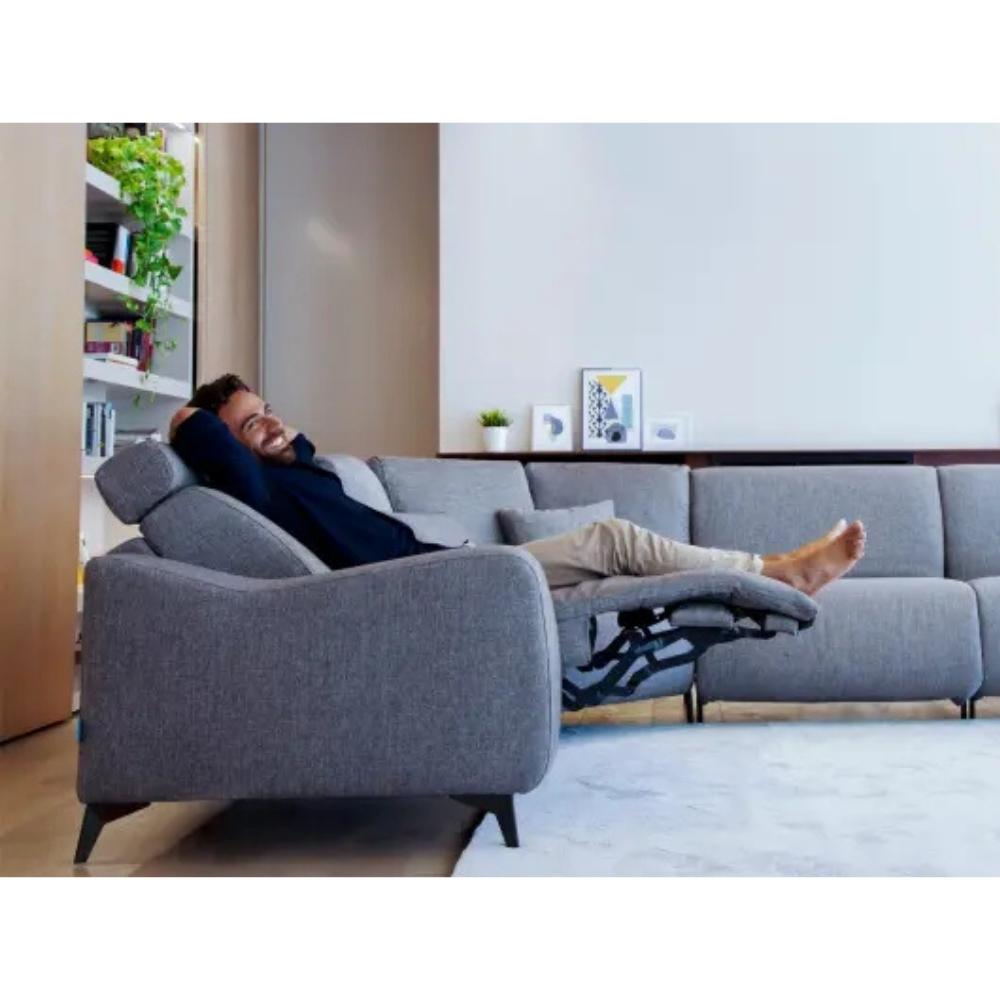 A man reclining comfortably in a modern gray fabric sofa with an extended footrest in a bright living room setting.
