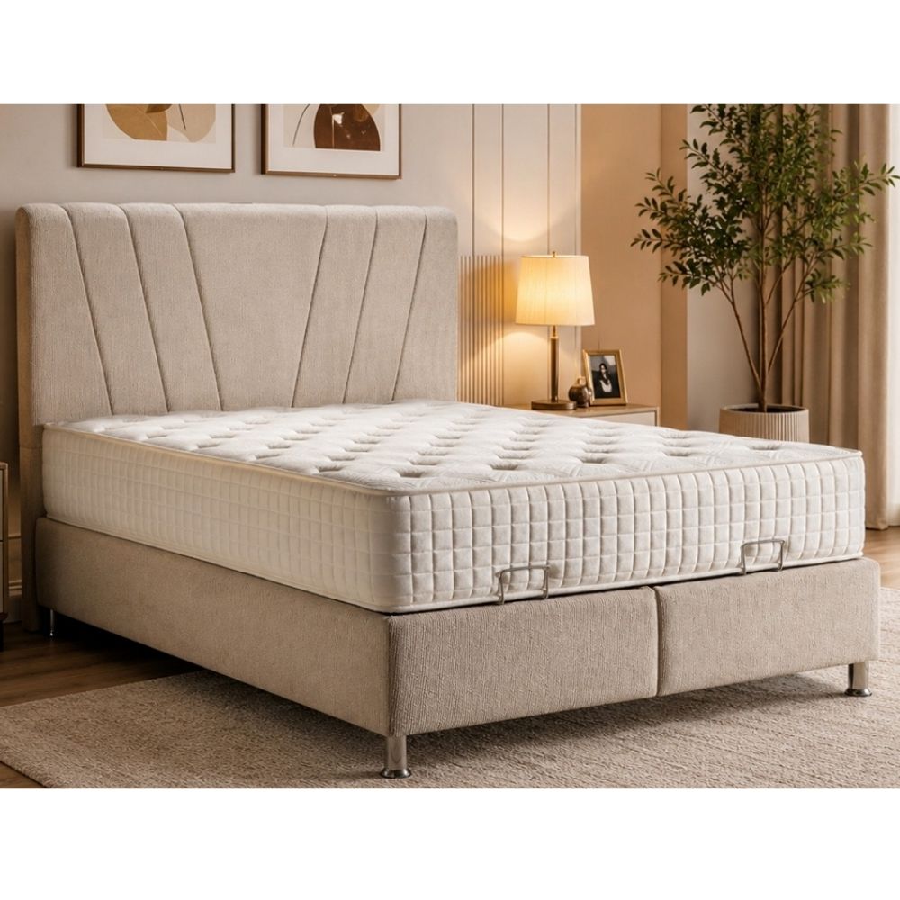 A beige upholstered ottoman divan bed frame with a matching tufted headboard and a white quilted mattress, shown in a styled bedroom setting with a lamp, framed wall art, and a potted plant.