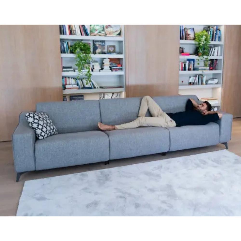 A man lies on a light gray three-seater sofa in a modern living room with built-in bookshelves and a white rug.