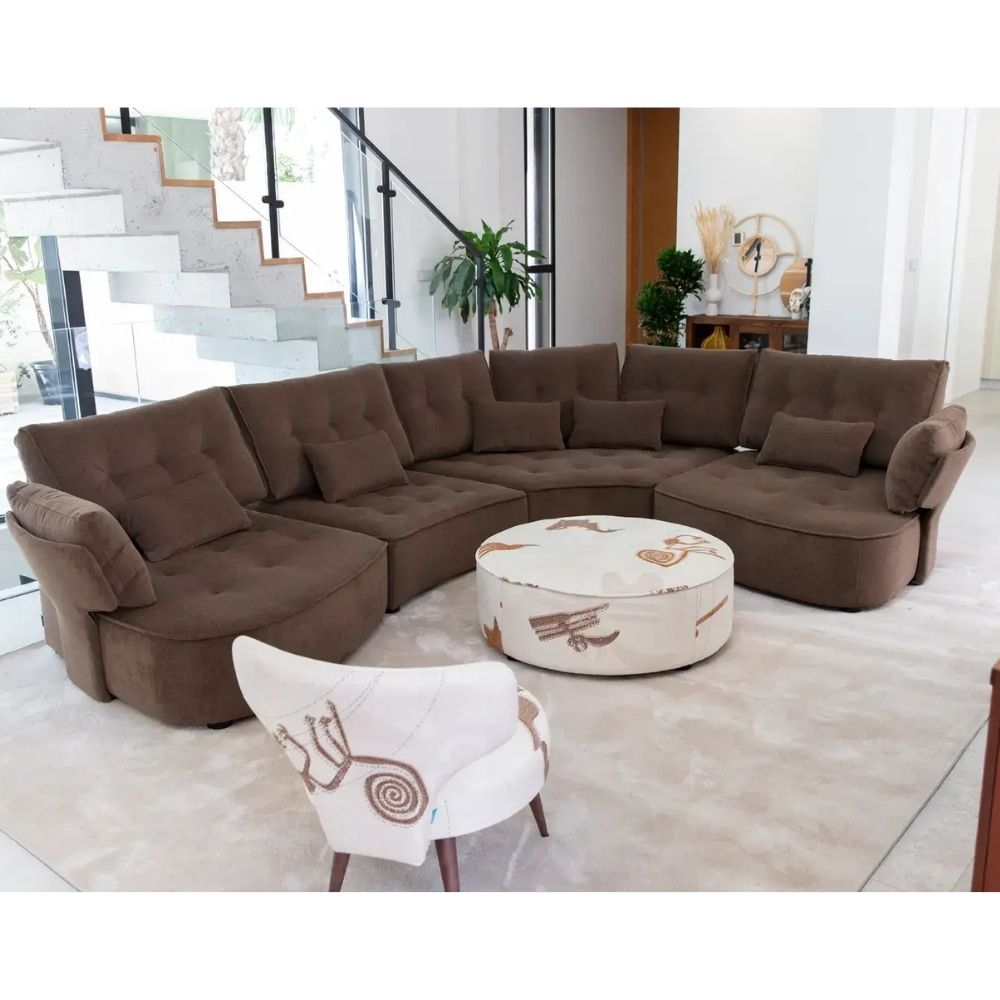 A curved brown sectional sofa in a modern living room setting, paired with a round ottoman and a white accent chair.
