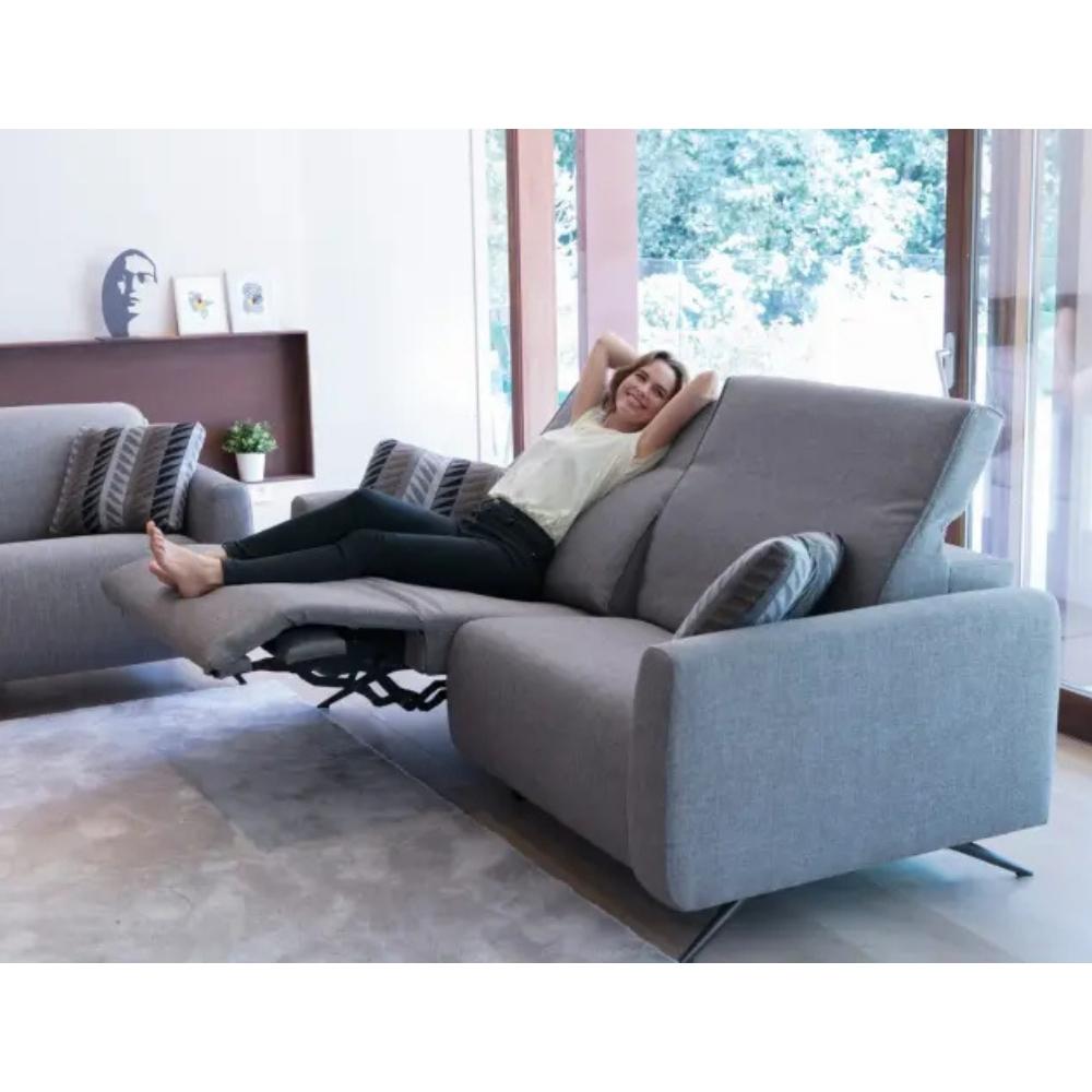 A woman reclines on a light gray upholstered sectional sofa with the footrest extended in a bright living room.