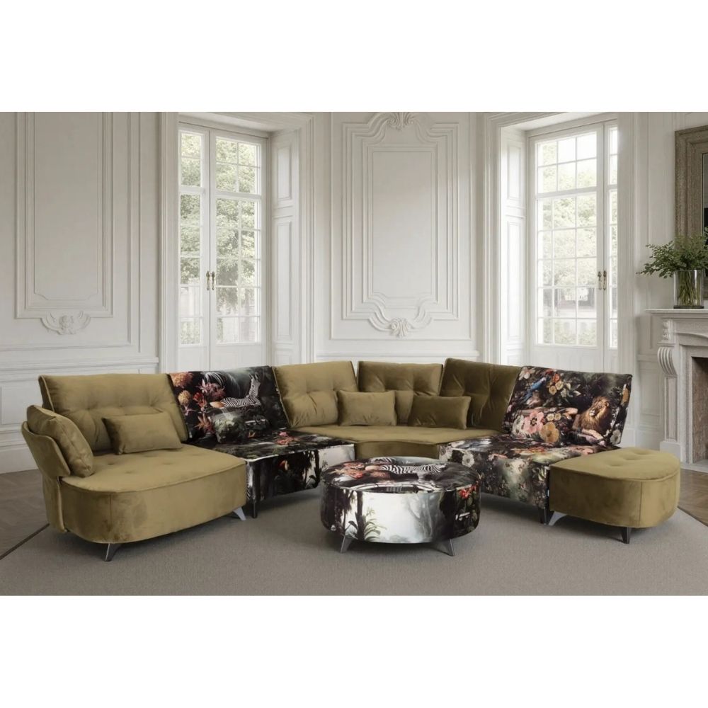 An olive green sectional sofa set with floral-patterned accent cushions and a matching round coffee table, staged in a bright, classic white room with high windows and a fireplace.