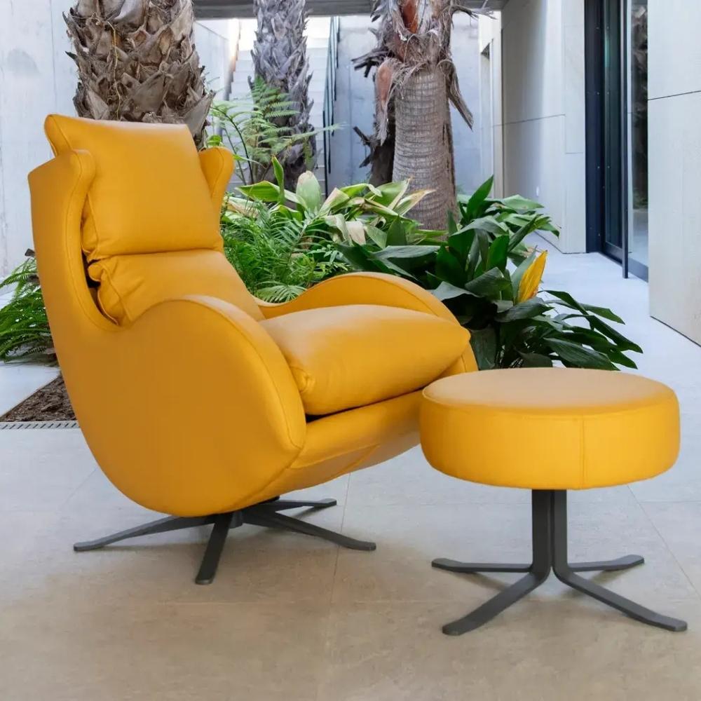 A modern yellow leather swivel lounge chair with a matching round footstool, set in a patio environment with potted plants and palm trees.