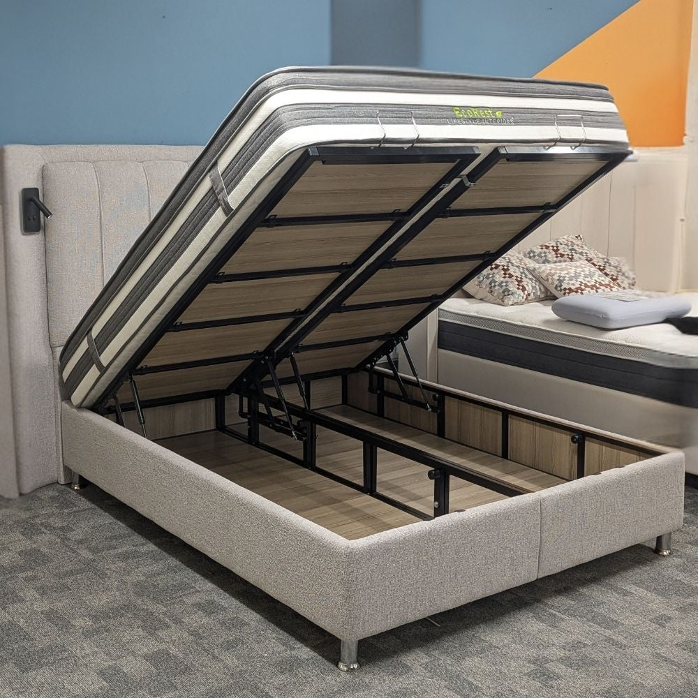 Grey upholstered ottoman bedframe, lifted to show storage space,  with a mattress and built in LED reading lights on a white background