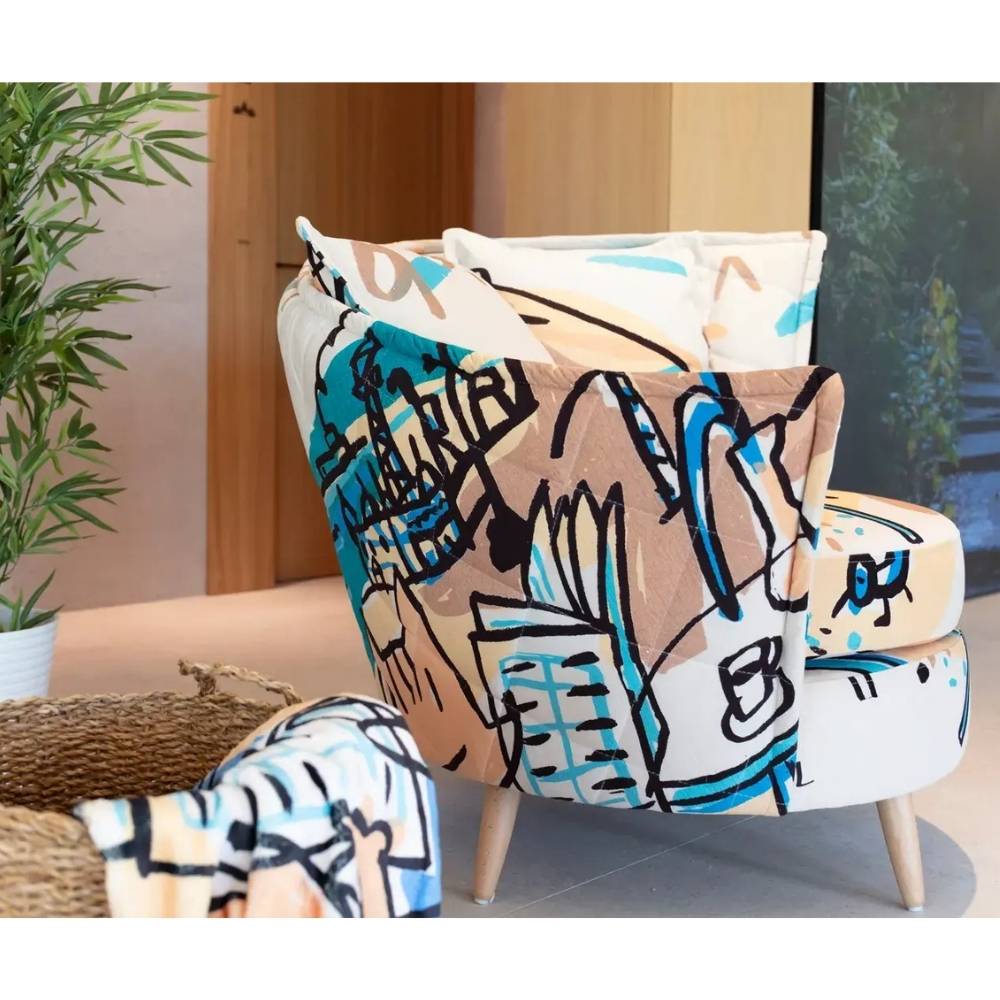 A modern upholstered armchair with a colorful graffiti-style abstract print in beige, white, blue, and black, shown in a styled interior setting.