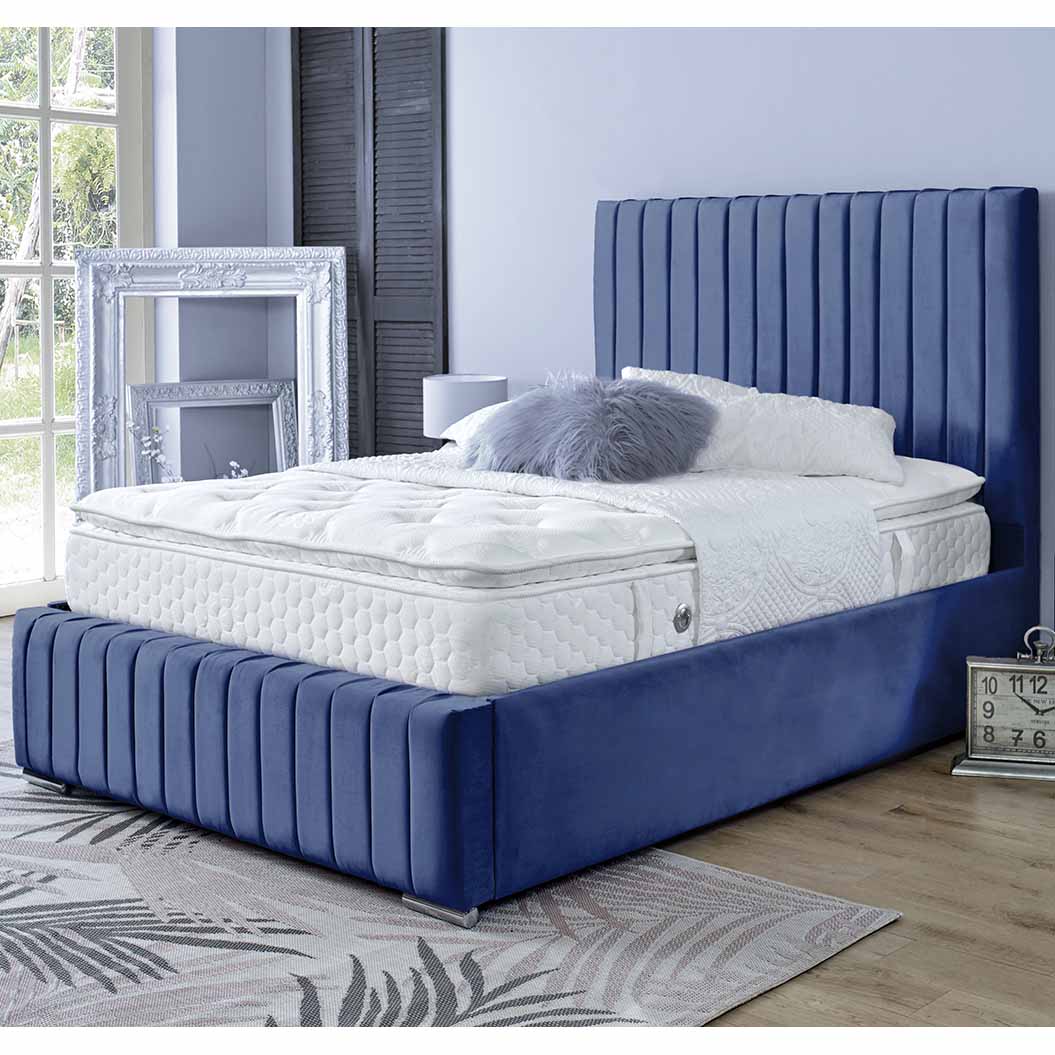 Blue upholstered bed with white mattress in a room with large windows and decorative elements.