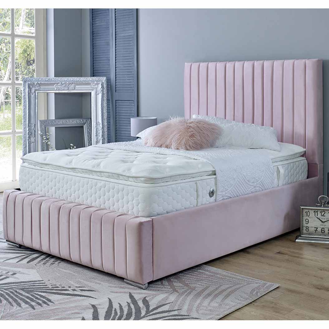 Pink upholstered bed with white mattress in a room with large windows and decorative elements.