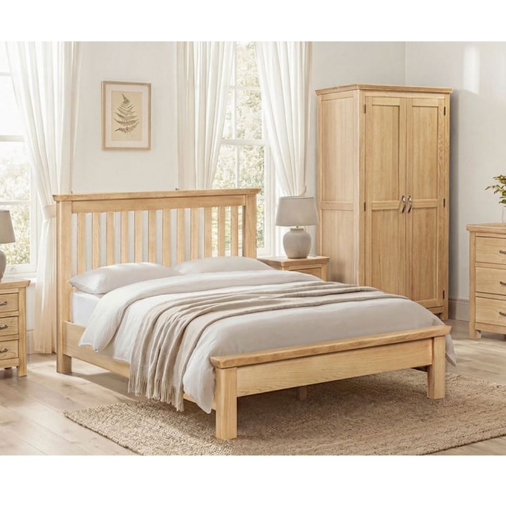 A light natural wood bed frame with a slatted headboard and footboard, styled in a bright, neutral-toned bedroom with white bedding, a matching wooden wardrobe, and bedside tables.
