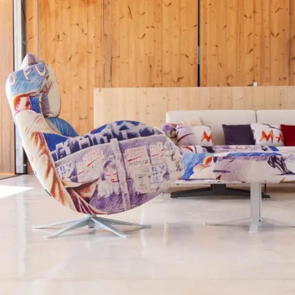 A modern lounge chair with a colorful patchwork print featuring vintage newspaper and poster designs, shown in a contemporary living room setting with a wooden wall background.
