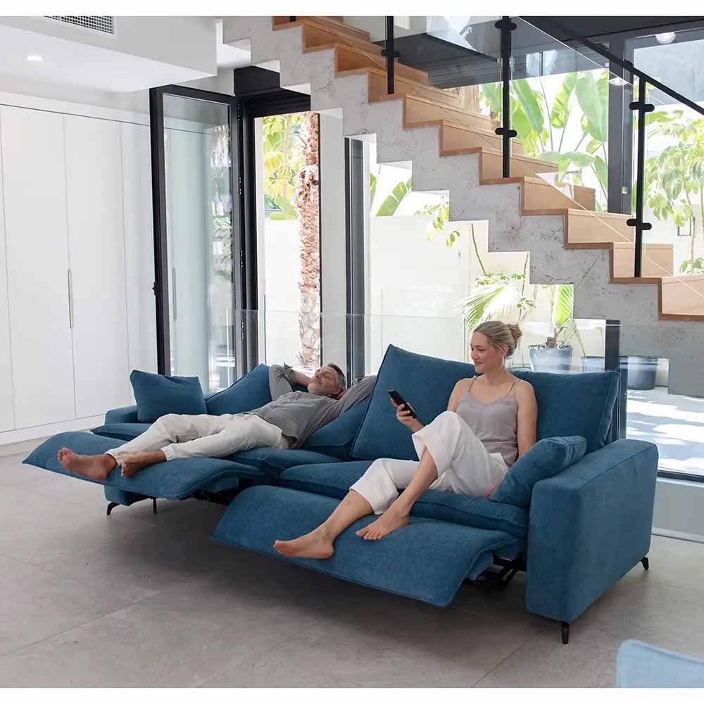 Two people relaxing on a blue reclining sectional sofa in a modern living room.