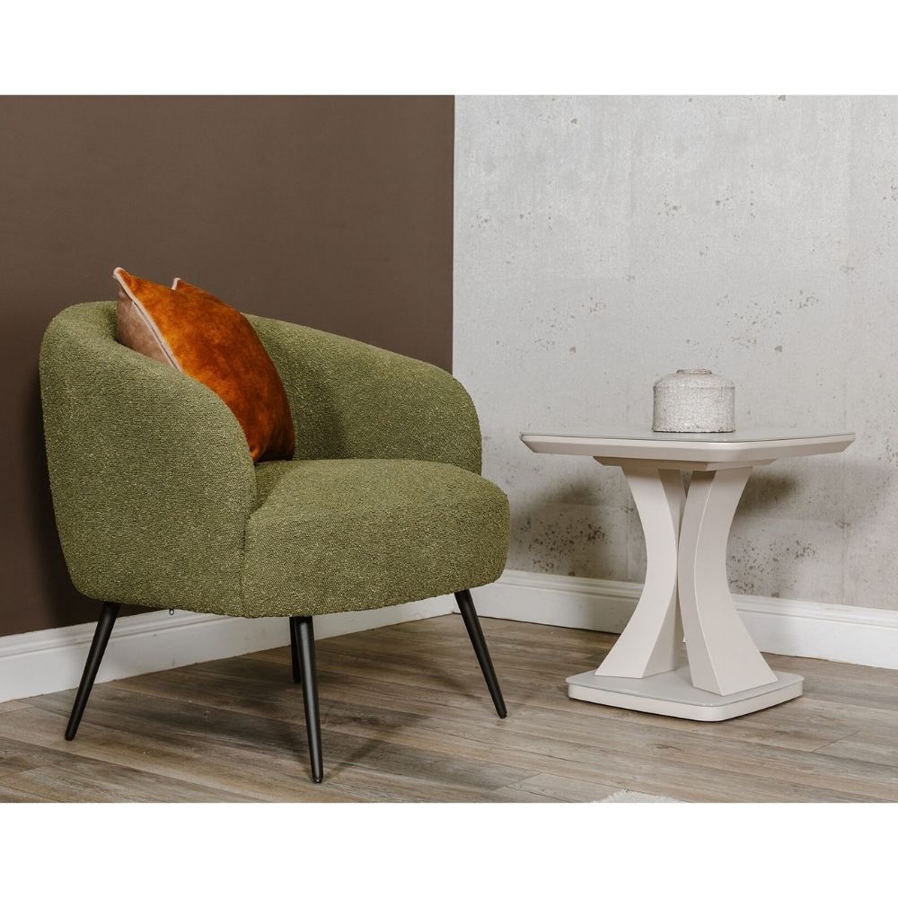 An olive green boucle armchair with black legs next to a white side table, set against a split brown and gray wall.