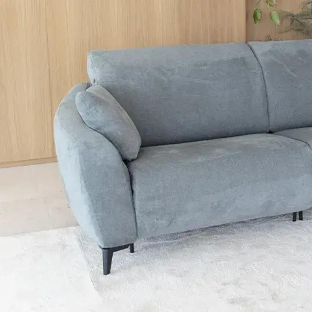 A modern two-seater sofa upholstered in a textured light gray fabric, shown in a minimalist room setting with a light wood paneled wall and a white rug.