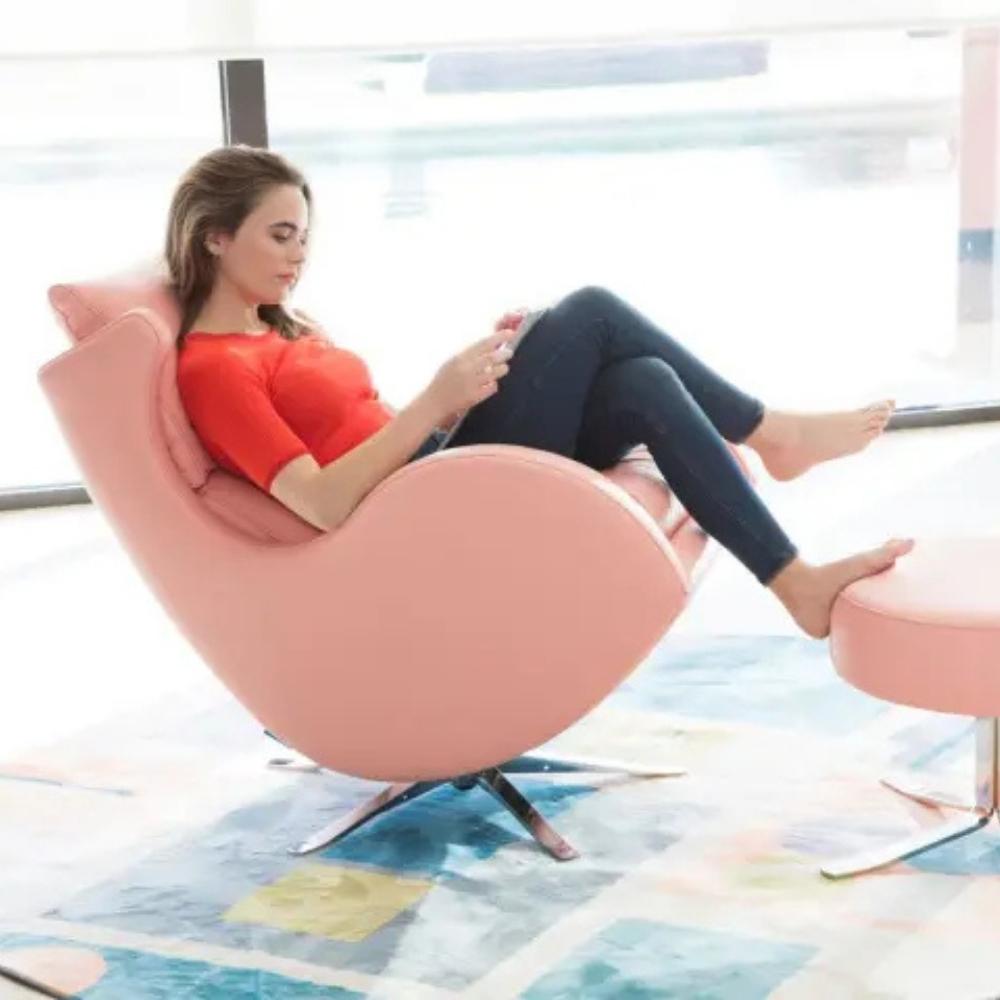 A woman reclining in a pink egg-shaped lounge chair with a matching footstool in a bright modern room.