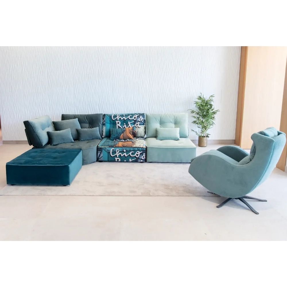 A modern living room setup featuring a sectional sofa in shades of teal and blue with patterned accent pillows and a curved teal swivel armchair on a light beige floor against a textured white wall.