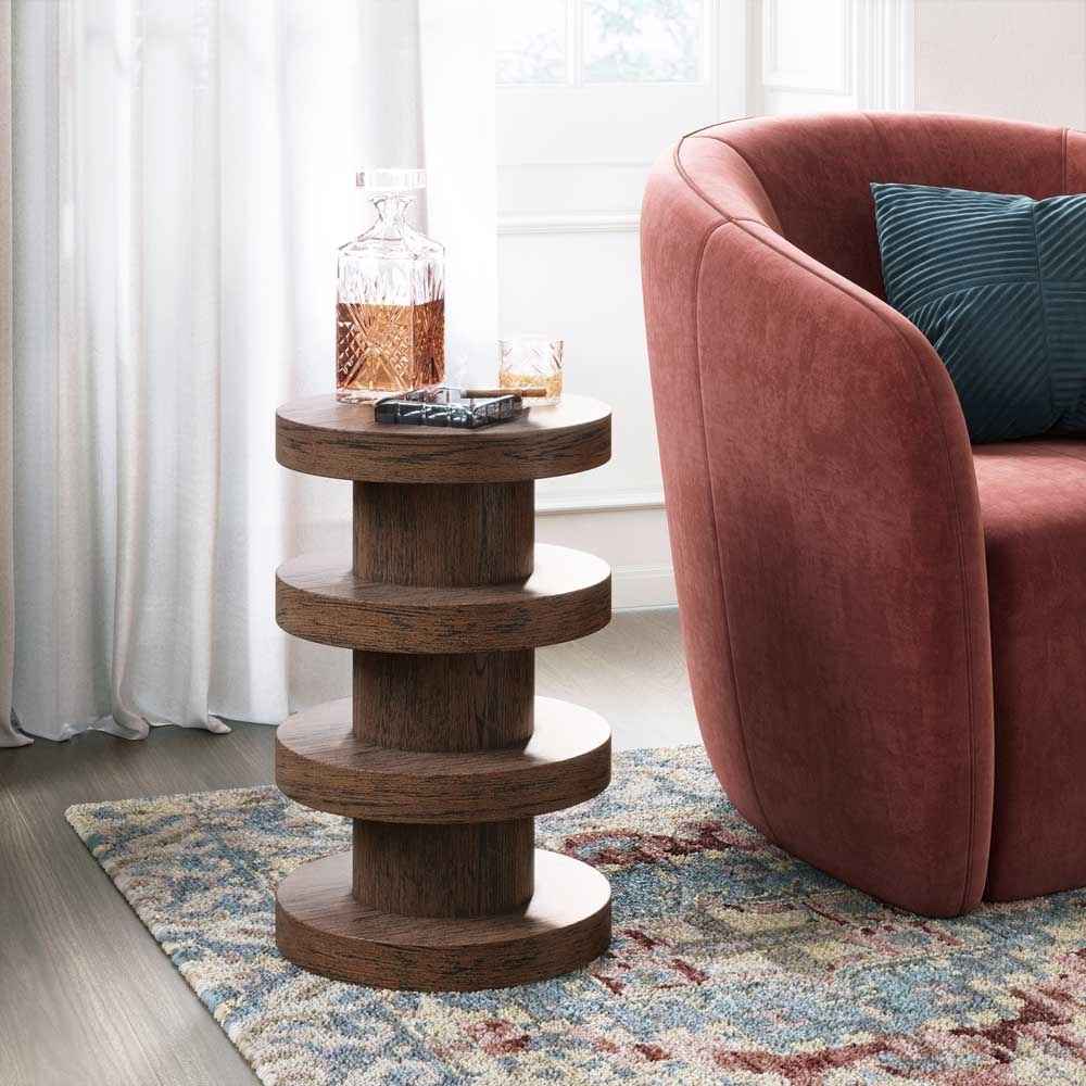 Wooden side table with a glass of whiskey next to a pink armchair with a blue pillow.