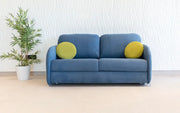 Blue sofa with yellow cushions in a room with a plant and white walls.