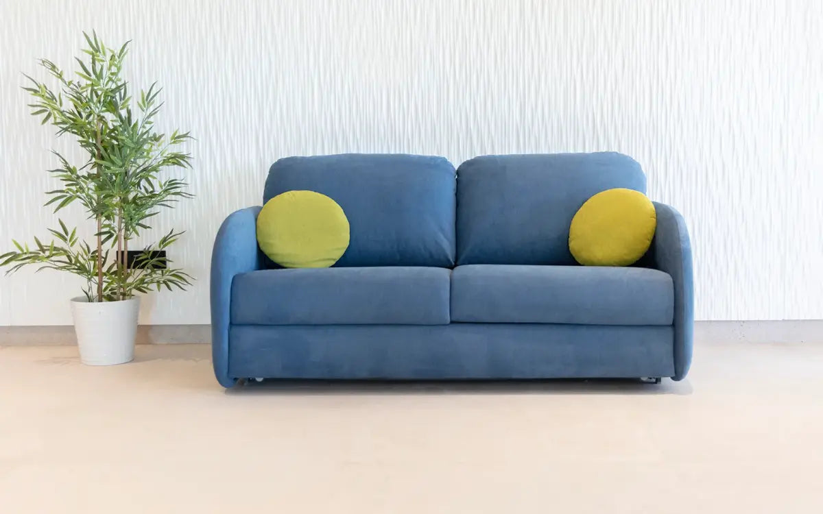 Blue sofa with yellow cushions in a room with a plant and white walls.