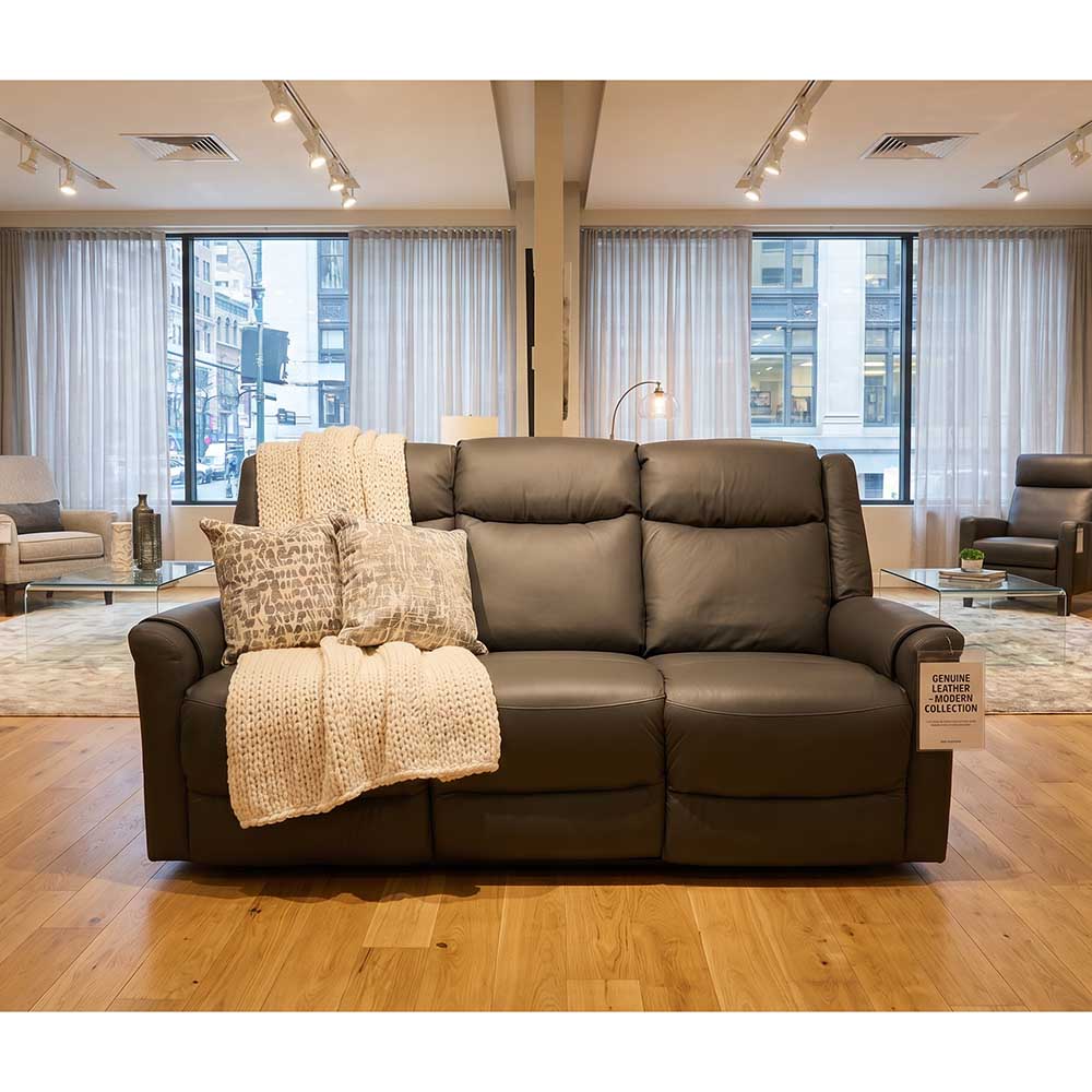 Grey leather electric reclining sofa in a modern furniture show room with large windows.