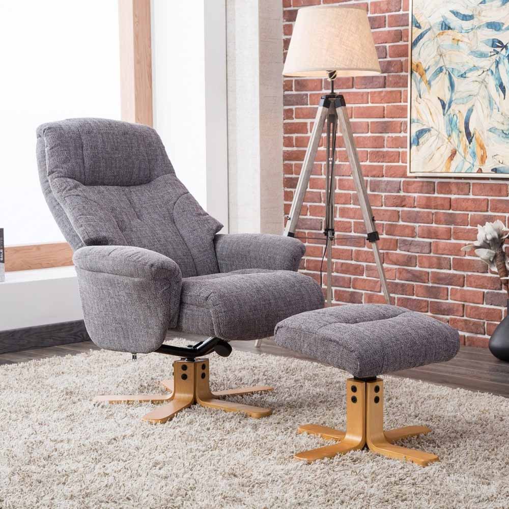 Gray recliner chair with footstool in a room with a brick wall and lamp.