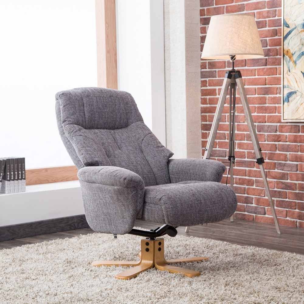 Gray recliner chair in a room with a brick wall and tripod lamp.