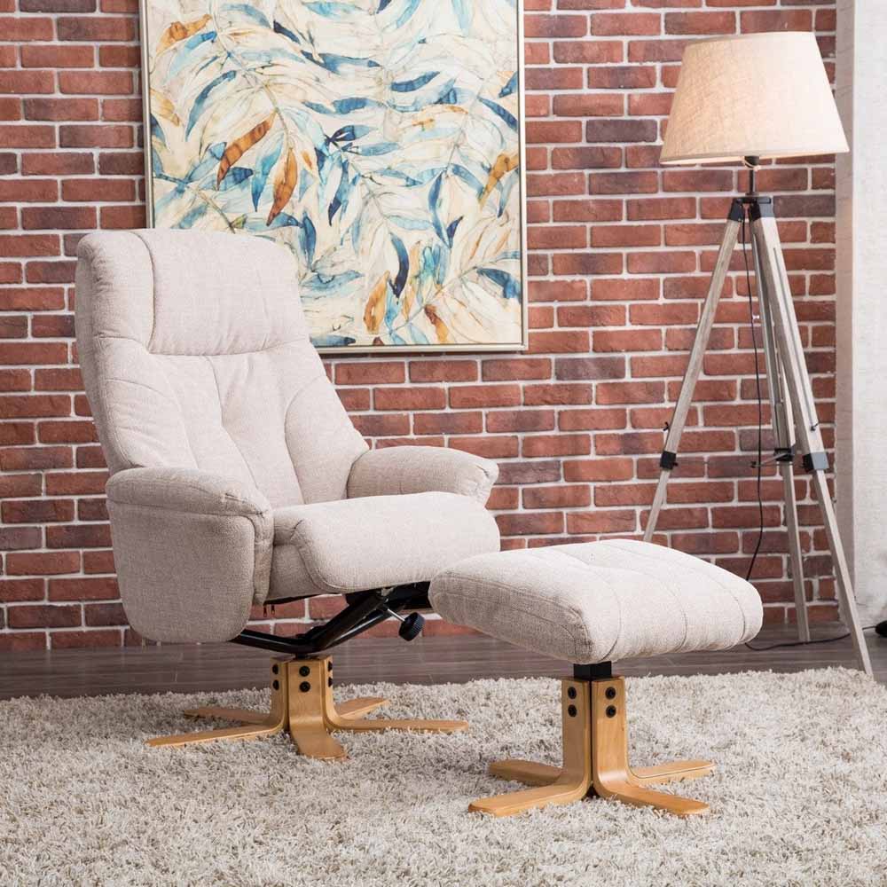 Wheat / beige recliner chair with footstool against a brick wall with a painting and lamp.