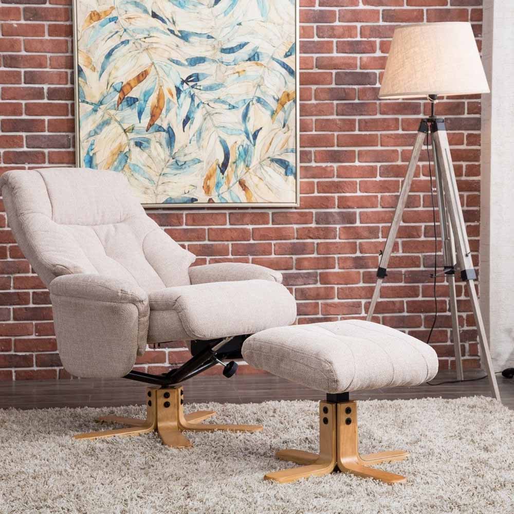 Wheat coloured recliner chair with footstool in front of a brick wall with a lamp and abstract painting.