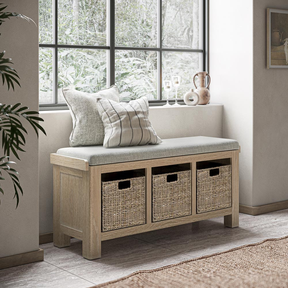 Wooden bench with storage baskets and cushions in a room with large windows.