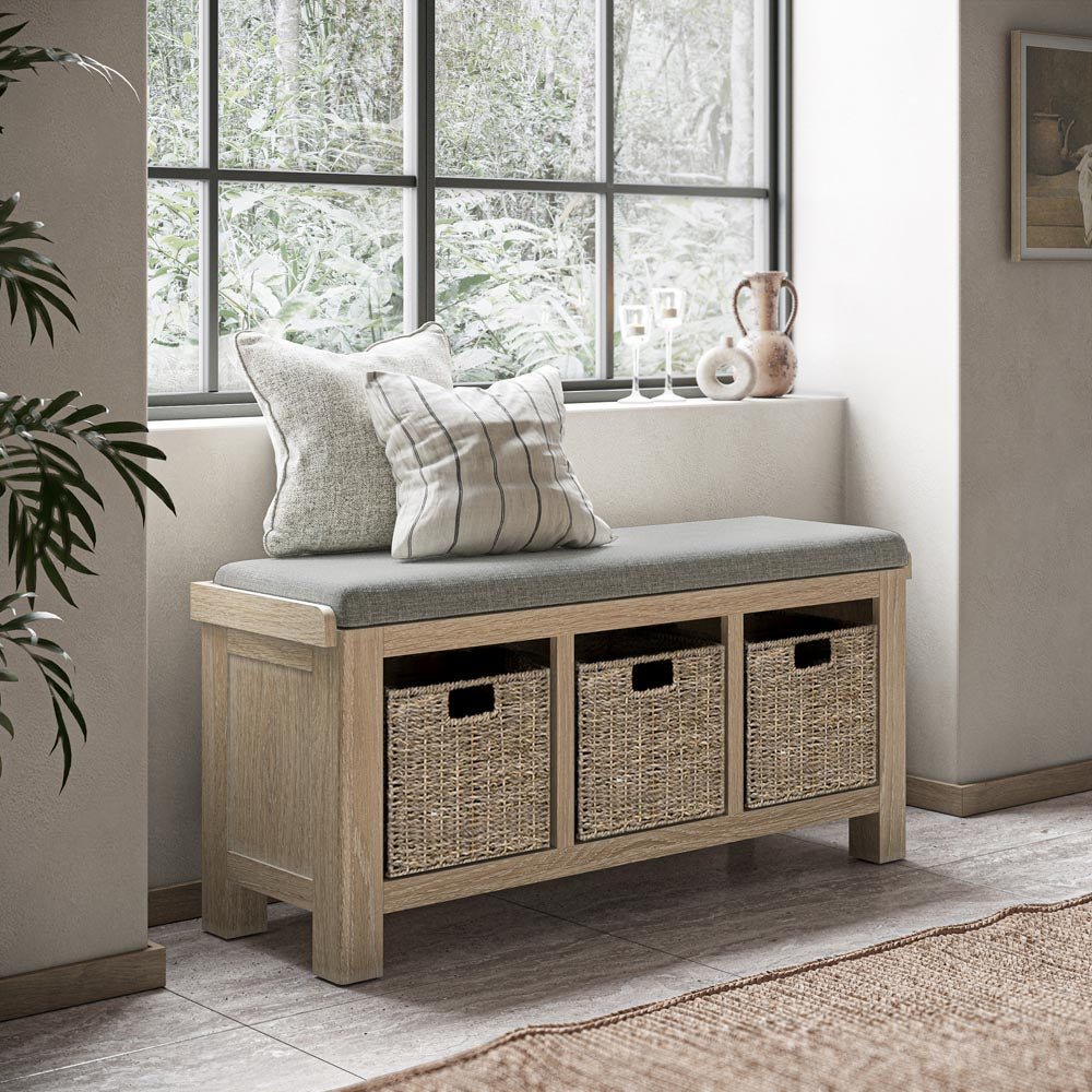 Wooden bench with storage baskets and cushions in a room with large windows.