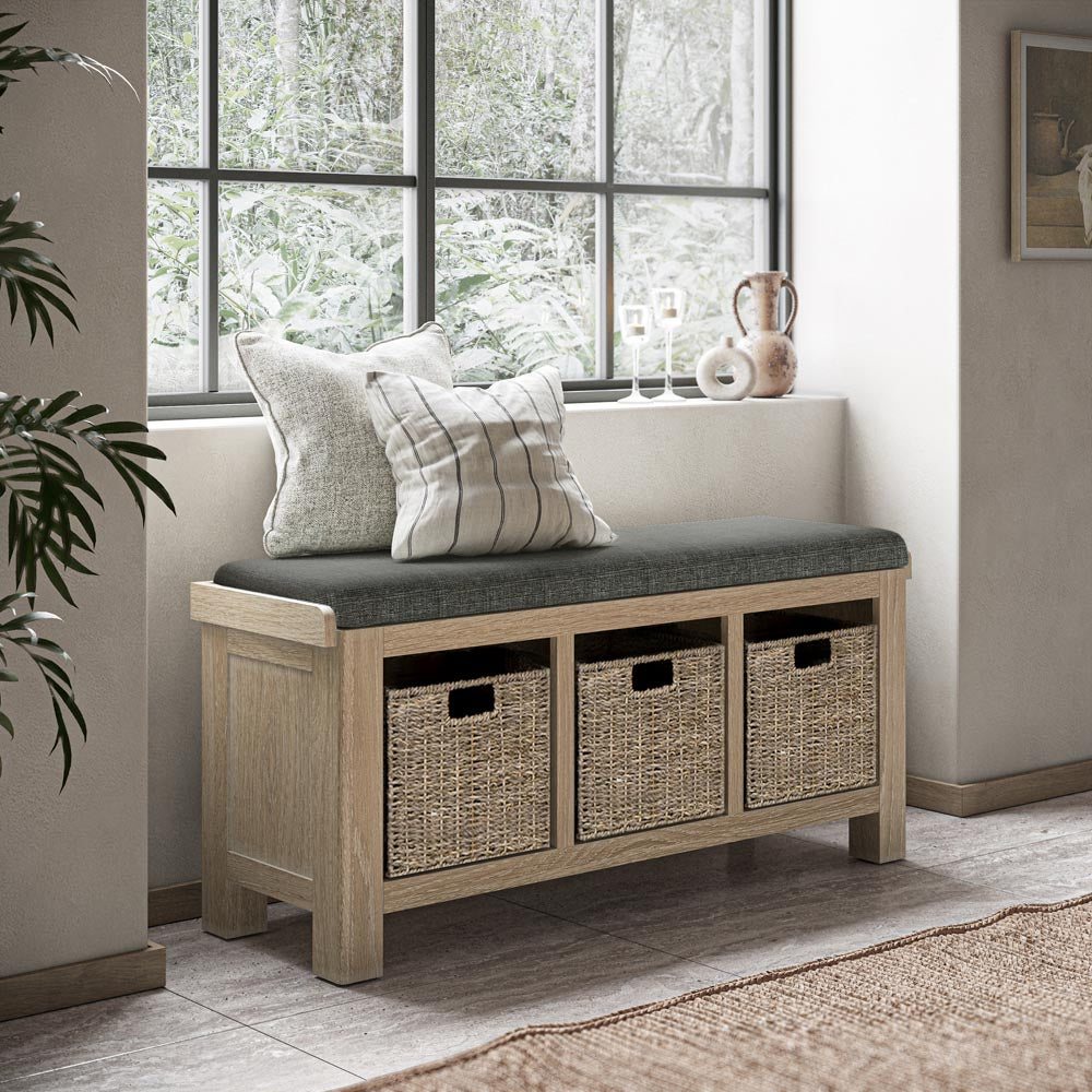 Wooden bench with storage baskets and cushions in a room with large windows.