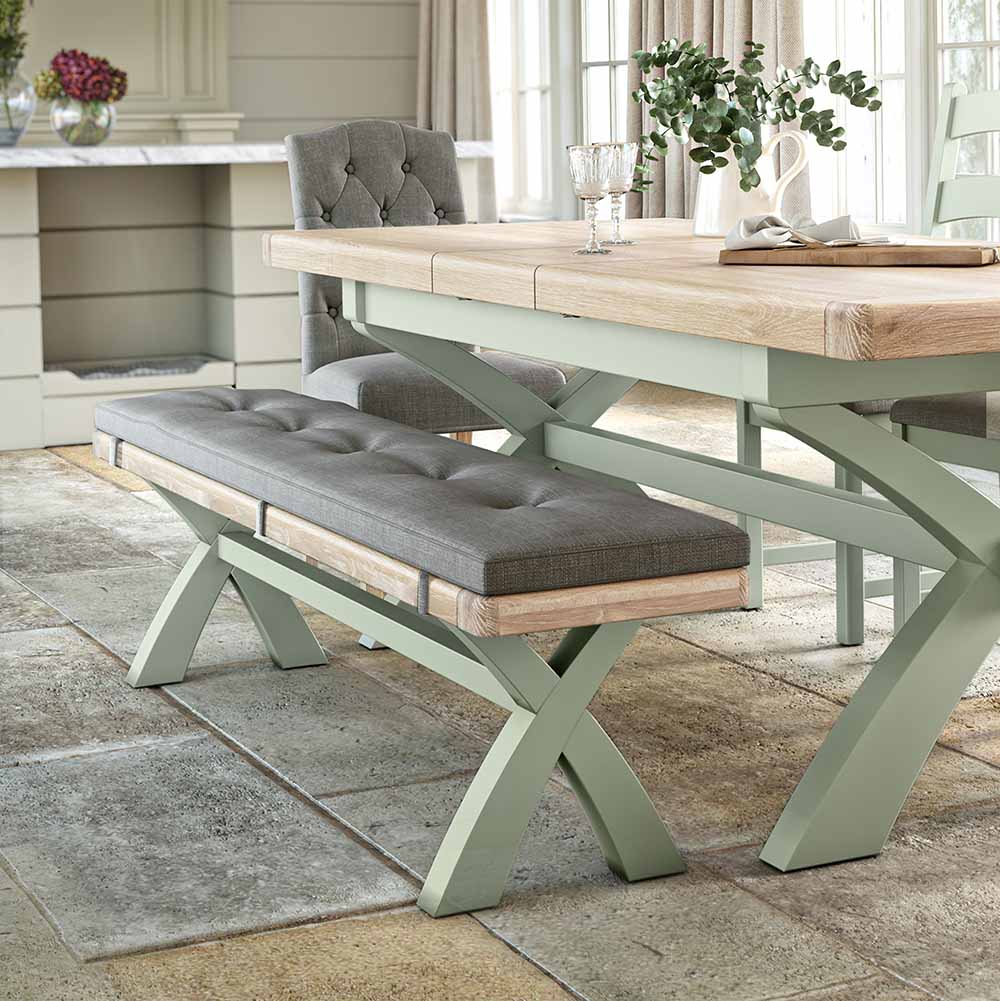 Long oak dining bench, painted sage with a grey coloured cushion. The bench is shown next to a matching table for reference / inspiration