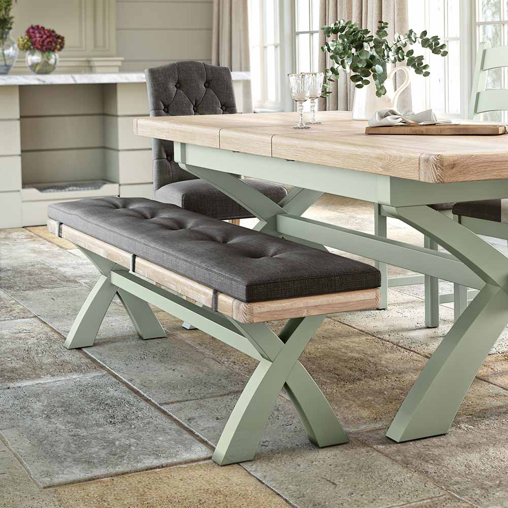 Long oak dining bench, painted sage with a charcoal grey coloured cushion. The bench is shown next to a matching table for reference / inspiration