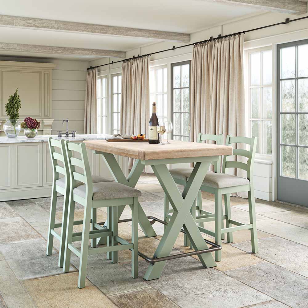 Sage painted oak Bar Table and 4 matching sage painted oak bar chairs set in a warm kitchen with floor to ceiling glass doors and cream curtains.