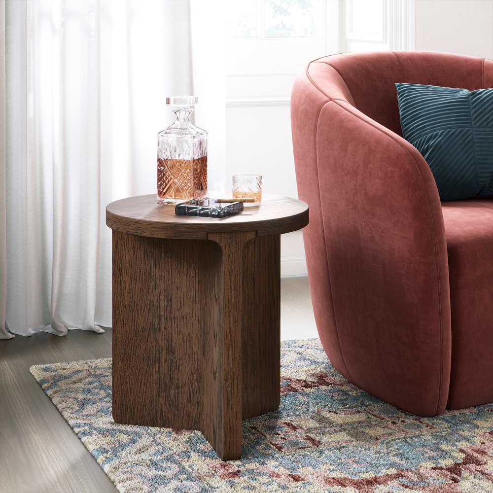Wooden side table with a bottle and glass next to a pink armchair with a blue cushion on a patterned rug.