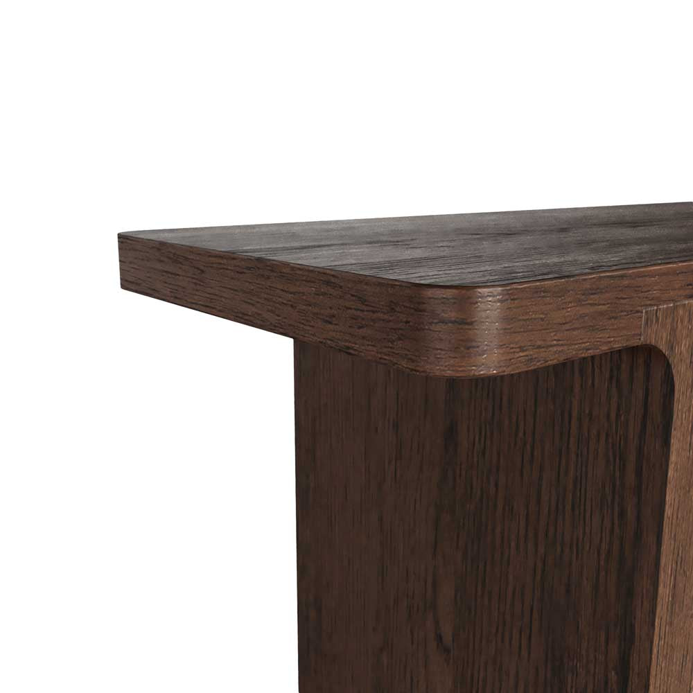 Close-up of a dark brown wooden console table corner showing the thick rounded apron and wood grain texture against a plain white background.
