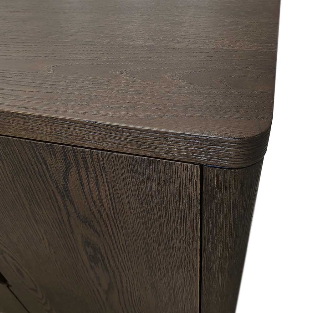 Close-up of a dark brown wood cabinet corner showing the grain texture, rounded top edge, and front door panel against a white background.