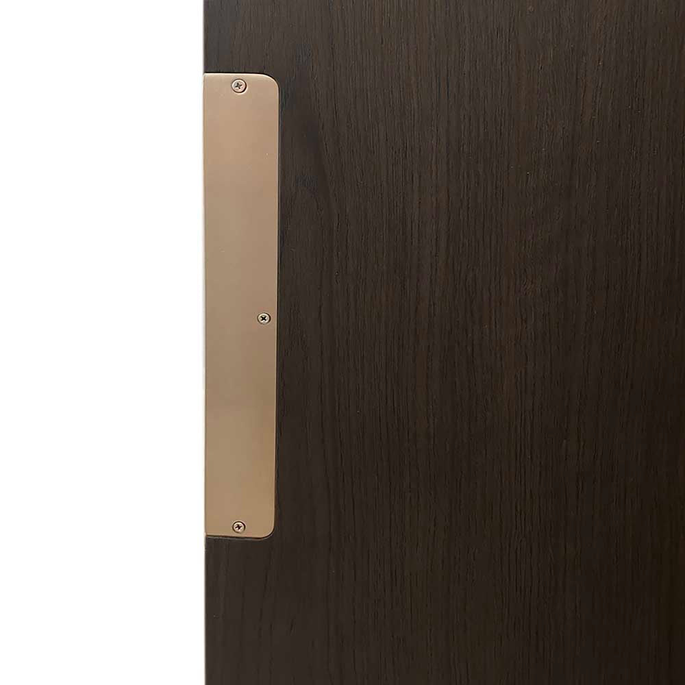 A close-up of a brushed brass or gold metal door pull handle mounted on a dark brown wood grain door.