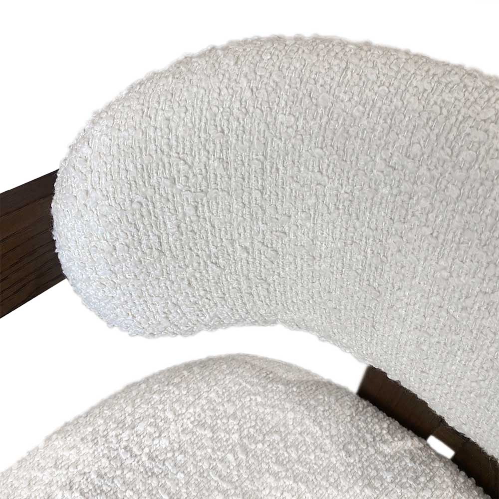 Close-up of a textured white bouclé upholstered chair cushion, showing the looped fabric texture and dark wood frame accents against a white background.