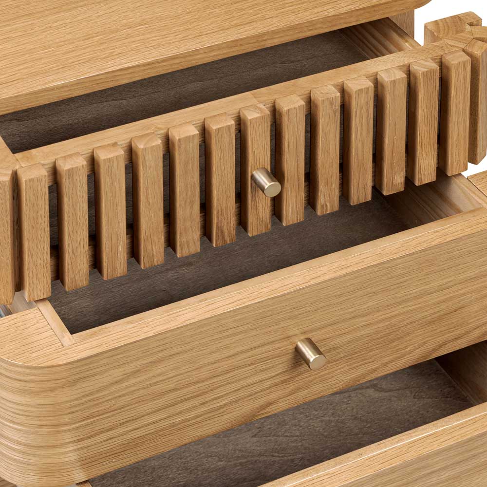 Partially open drawers of 3 drawer oak bedside locker. The top drawer has a slatted design and each drawer has a central gold effect handle