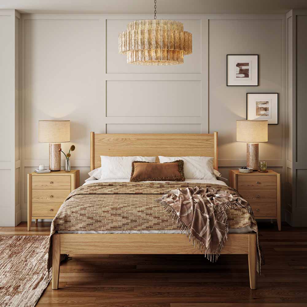 A warm, modern bedroom scene featuring a light oak wood bed frame with a matching headboard and footboard, styled with neutral-toned bedding, flanked by matching nightstands and lamps under a tiered chandelier.