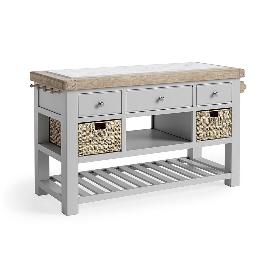 Oak Kitchen Island, oak and marble top. Underneath the storage has been broken into three section. First, 3 grey drawers, next, an open storage space flanked by a storage basket on either side, finally a completely open storage section with grey wooden slats. there is also a towel rail on the left side.