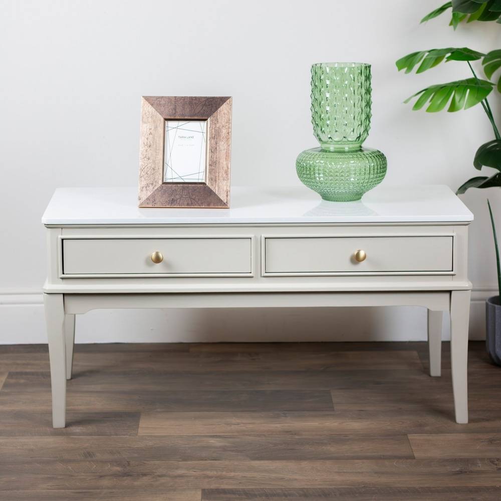 light beige / stone coloured coffee table with a green vase and framed picture on a wooden floor.