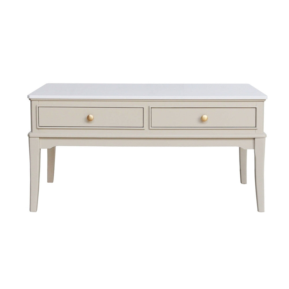 A light beige / stone coloured coffee table with two drawers and small round gold knobs, shown against a plain white background.