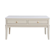 A light beige / stone coloured coffee table with two drawers and small round gold knobs, shown against a plain white background.