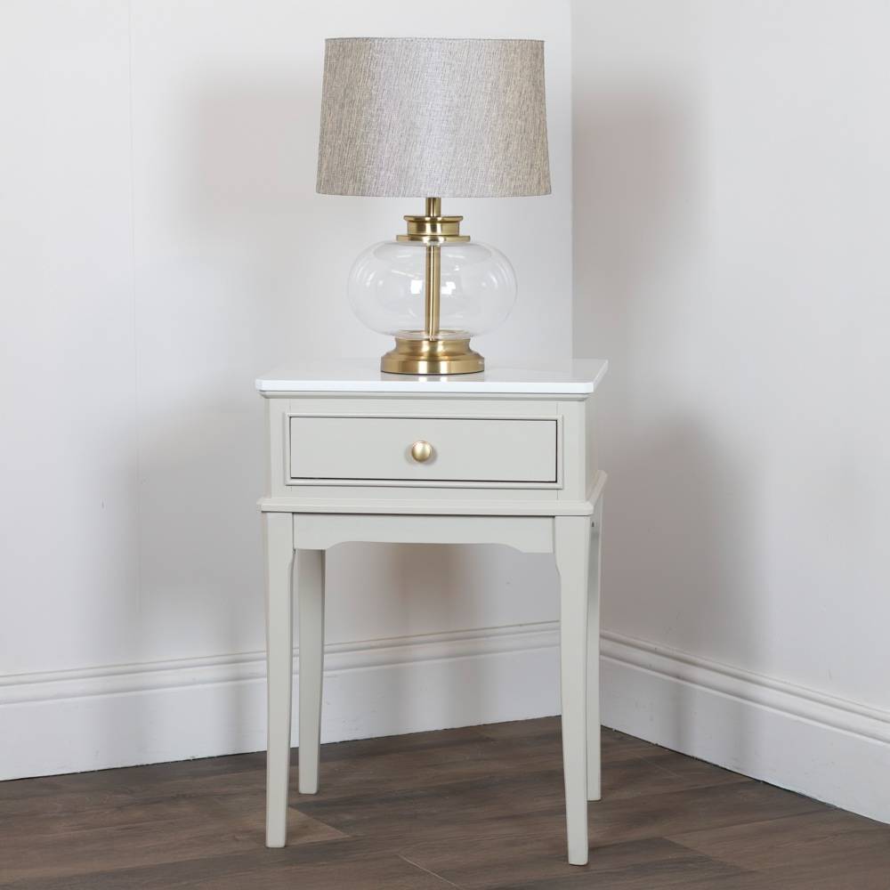 Stone / beige side table with a lamp on a plain wall background